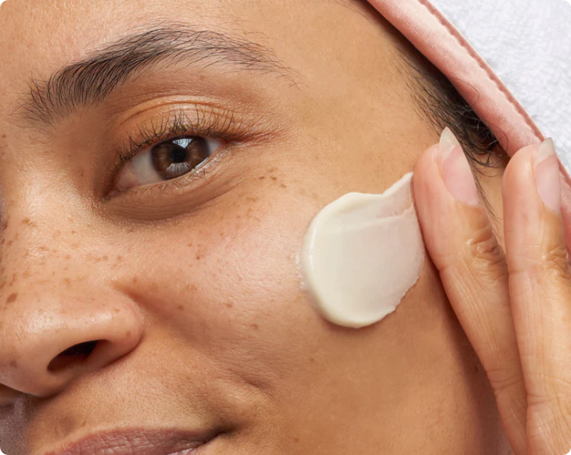 A woman applies cream to her face